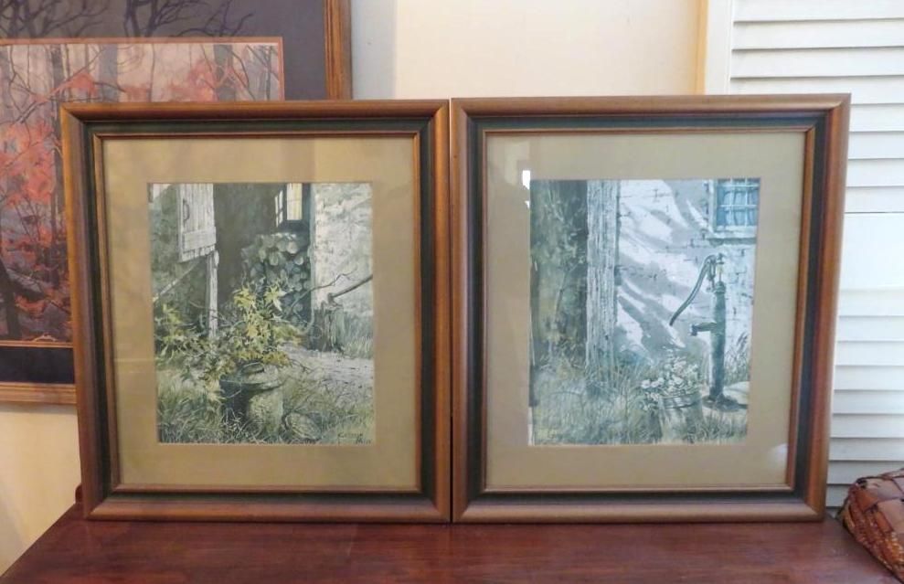 Two framed art prints of weathered buildings with vegetation and a water pump.