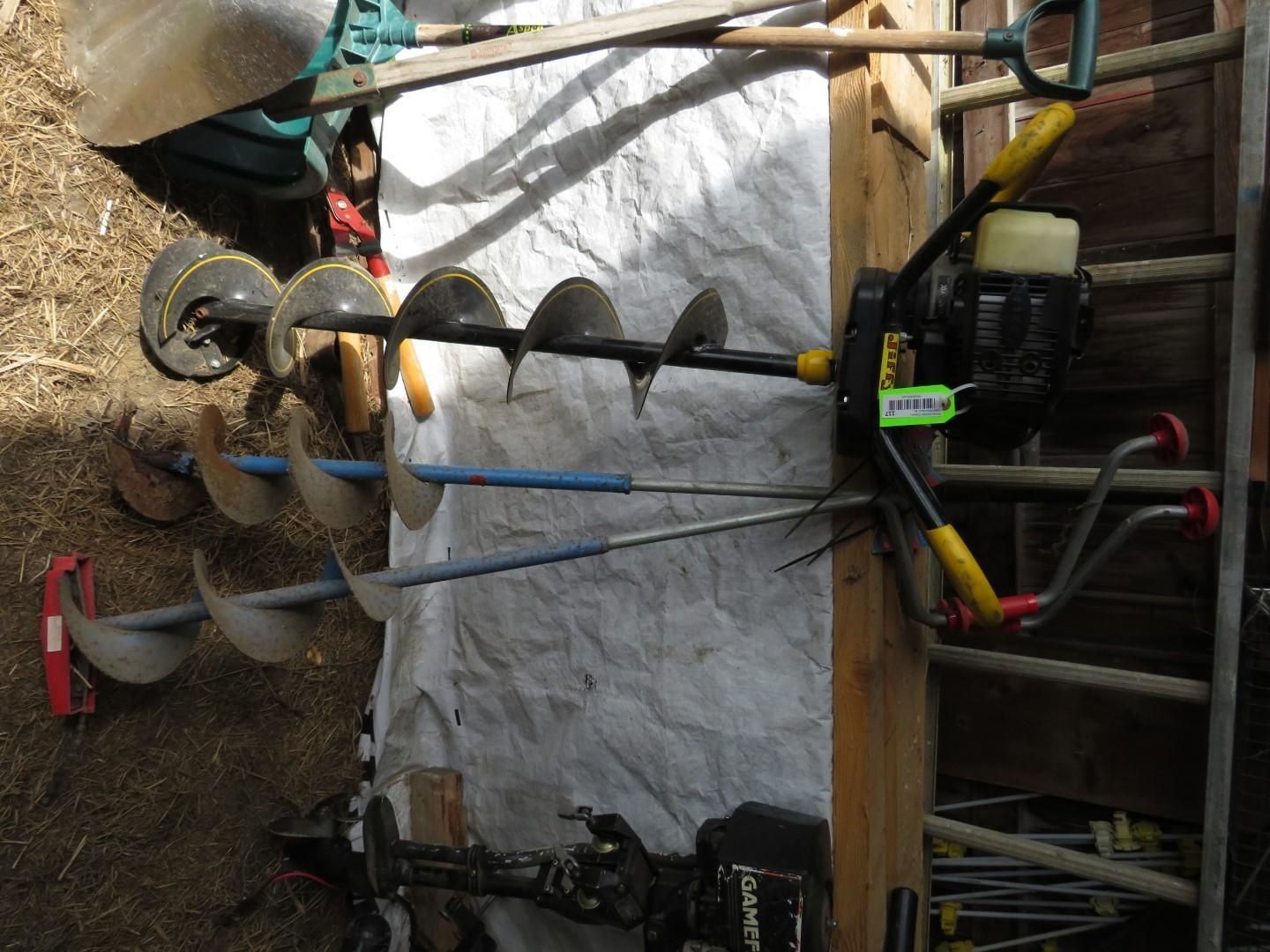 An auger with multiple drill bits leaned against a wooden structure.