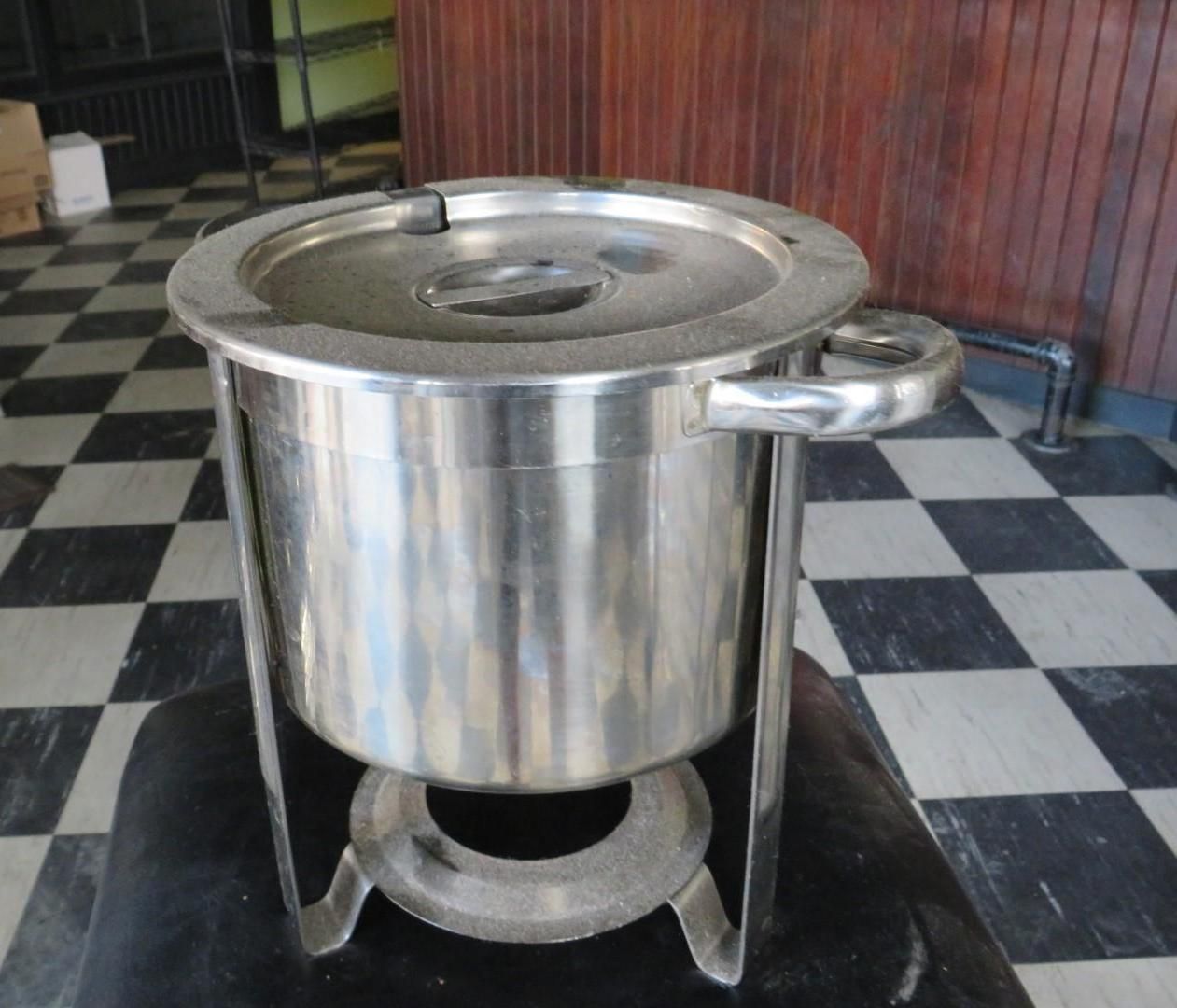 Stainless steel chafing dish with lid and stand, on a checkered floor.