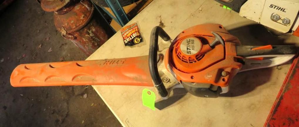 An orange Stihl chainsaw laying on a light-colored surface with a green tag.