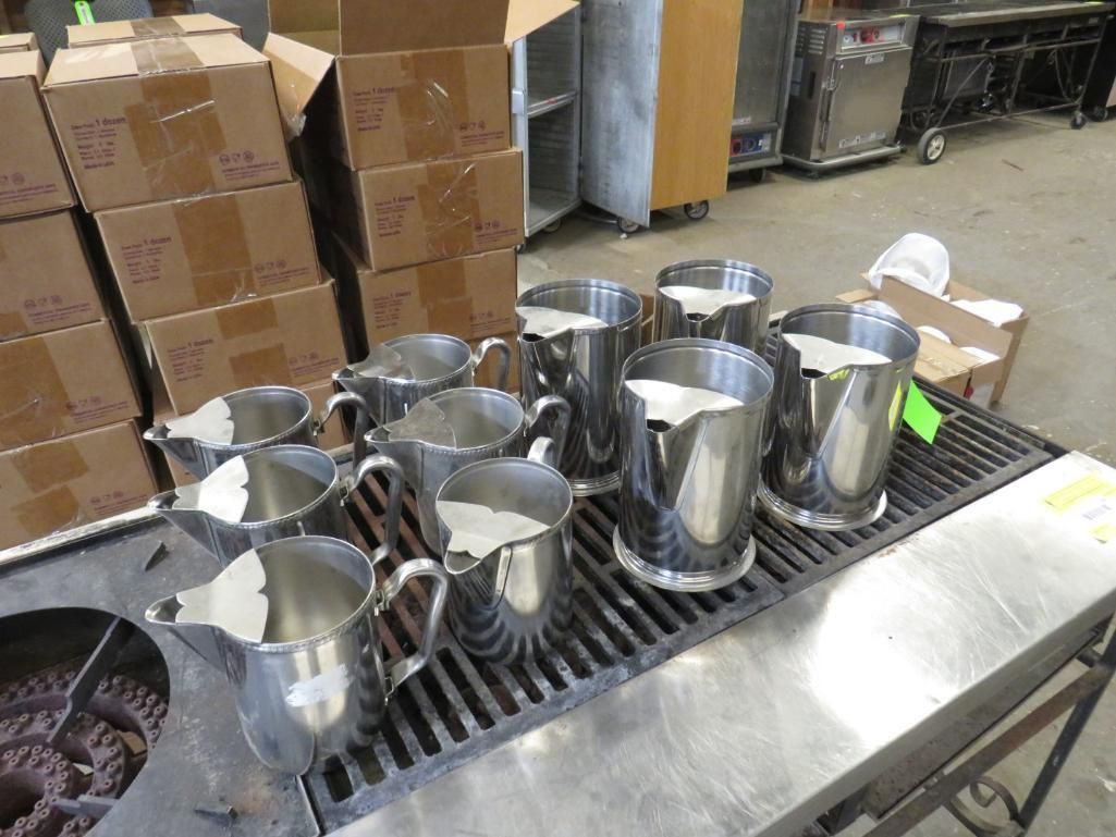Several shiny metal pitchers arranged on a griddle surface.