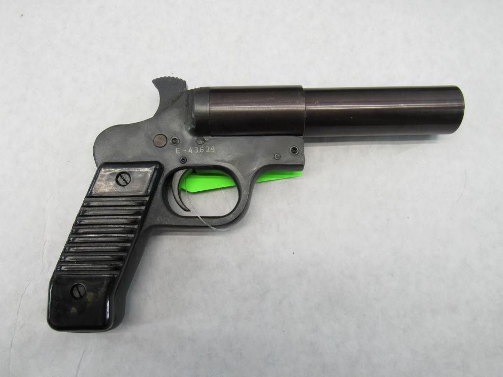 Flare gun, black with a ribbed grip, barrel pointing right, resting on a white surface.