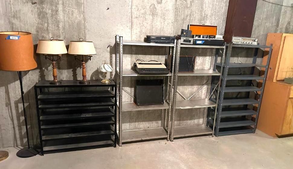 Basement storage: lamps, shelves with electronics, a cabinet against a concrete wall.