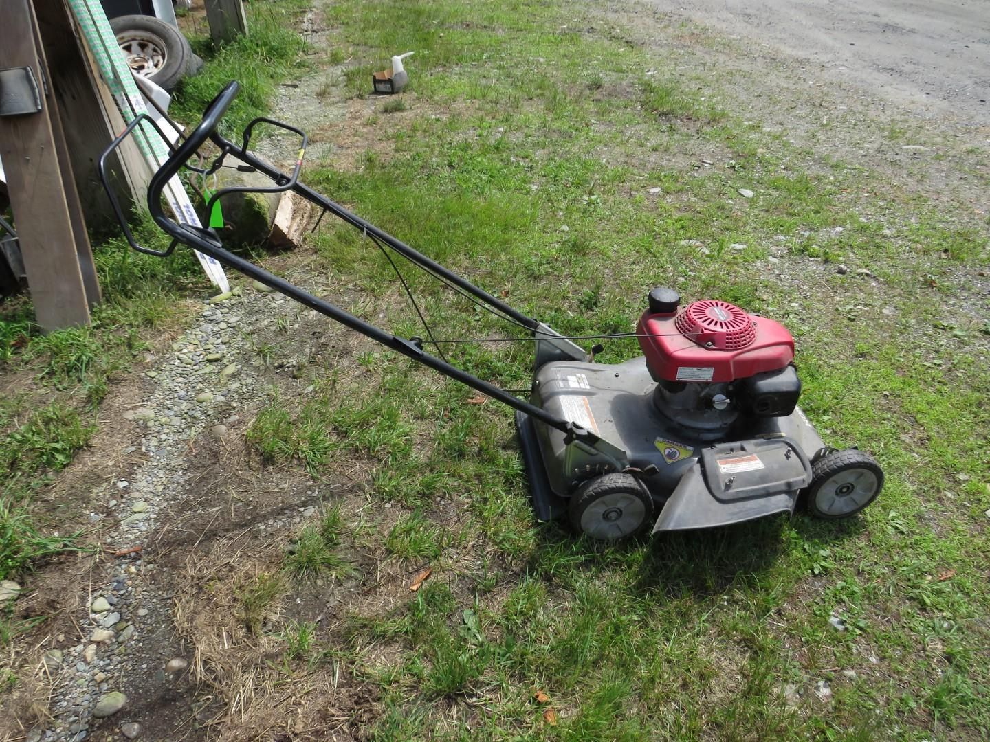 A red Honda lawnmower sits on green grass next to a gravel path.
