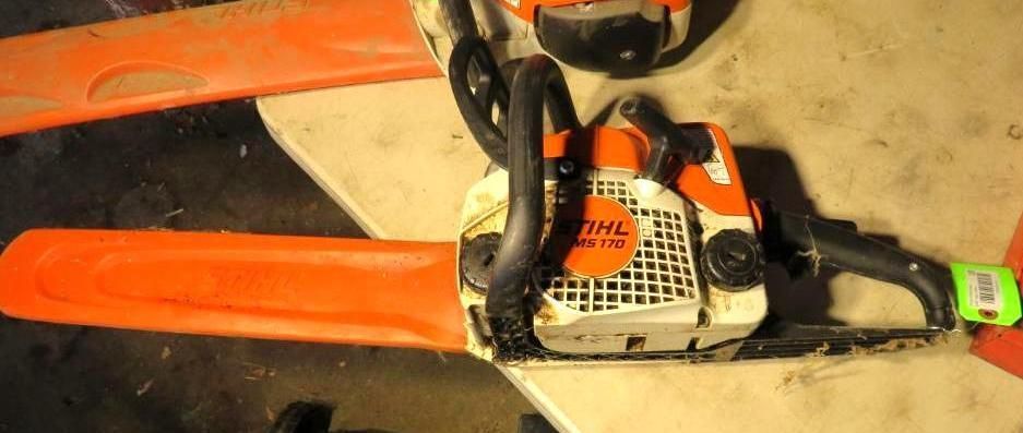Orange and white Stihl chainsaw with safety bar in a workshop setting.