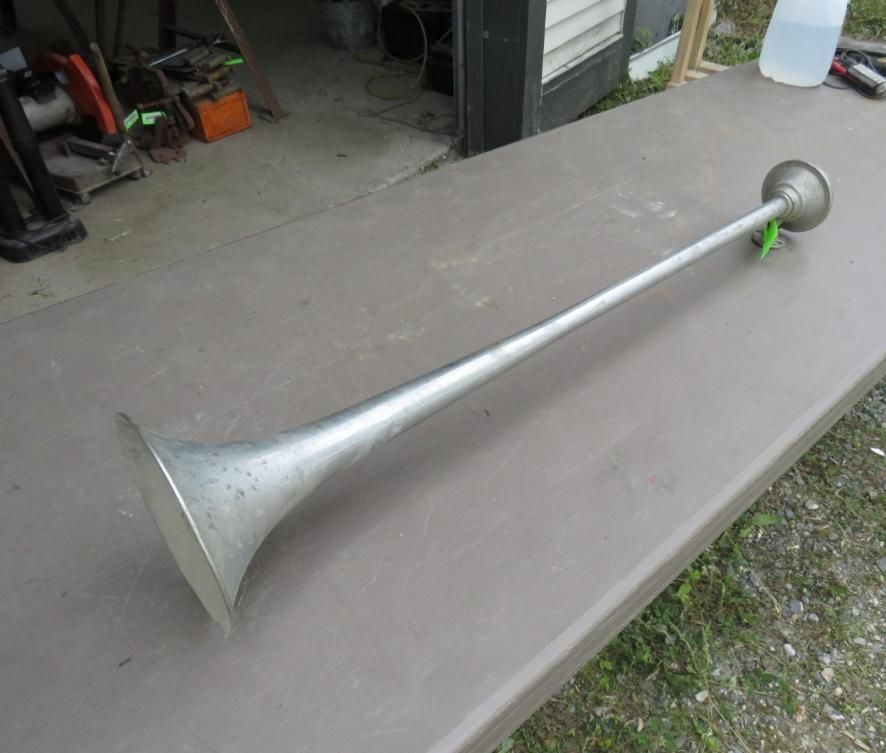Long, silver car horn on a brown table, outside.