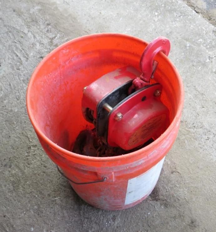 Red electric hoist inside an orange bucket, set on a concrete surface.