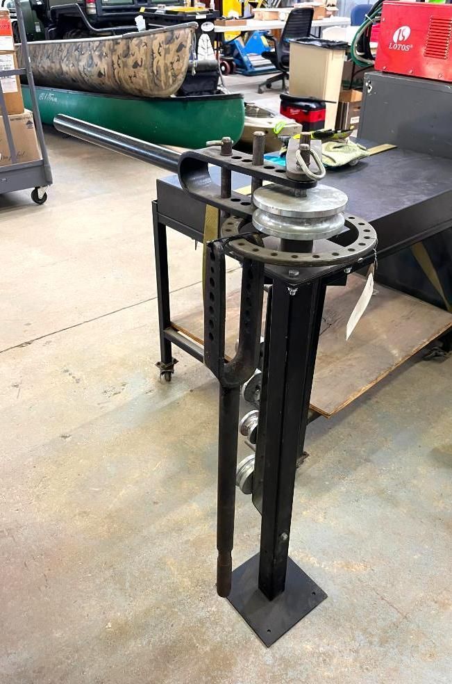Black metal tube bender on a workshop table.