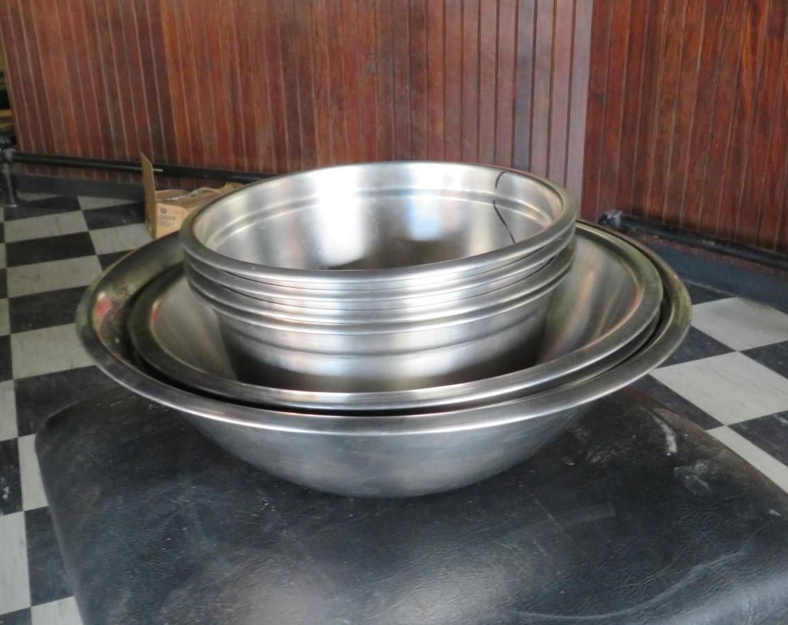 Stack of stainless steel mixing bowls on a black surface against a wood-paneled wall.