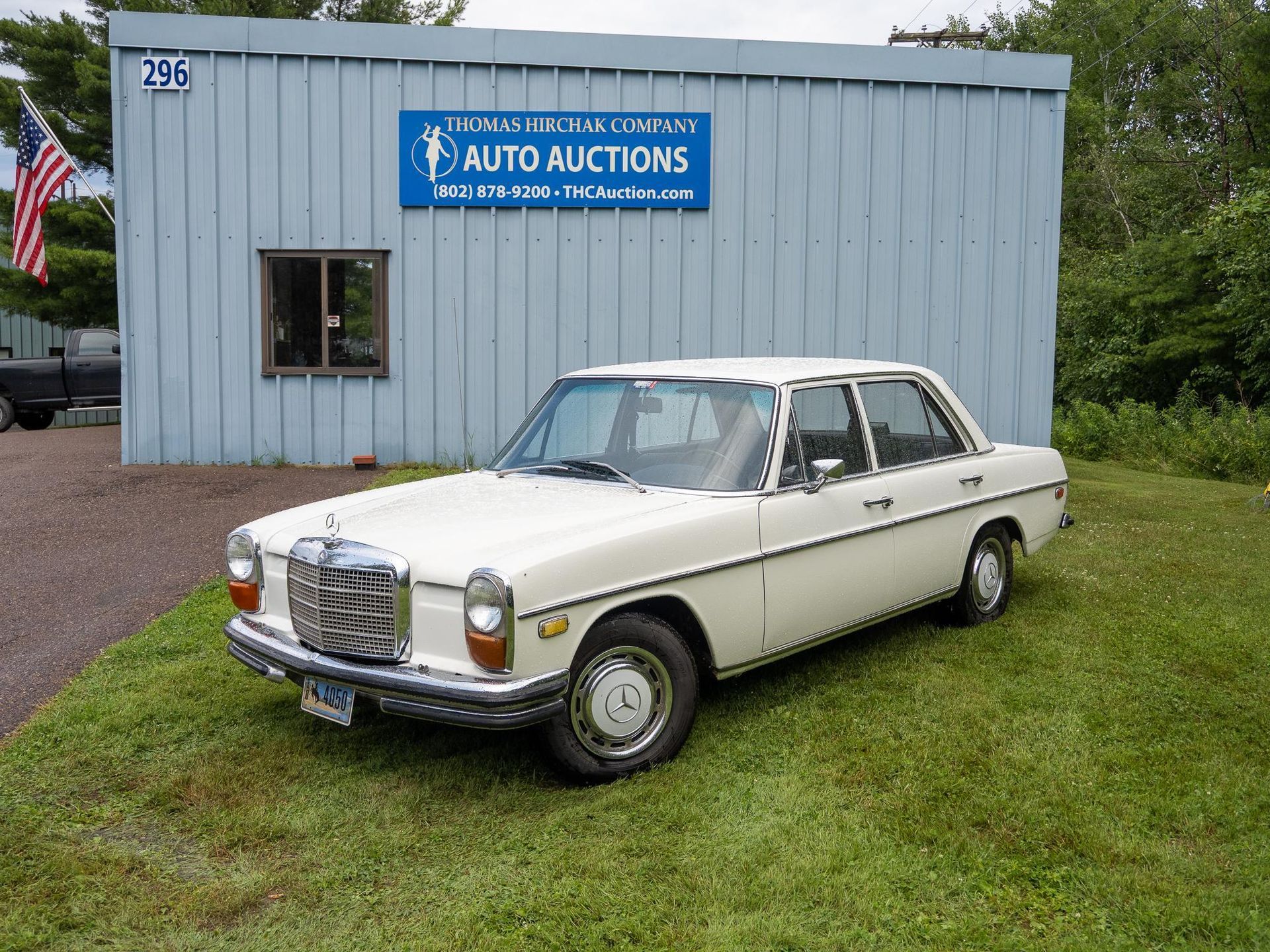 White vintage Mercedes sedan parked in front of an auto auction building.
