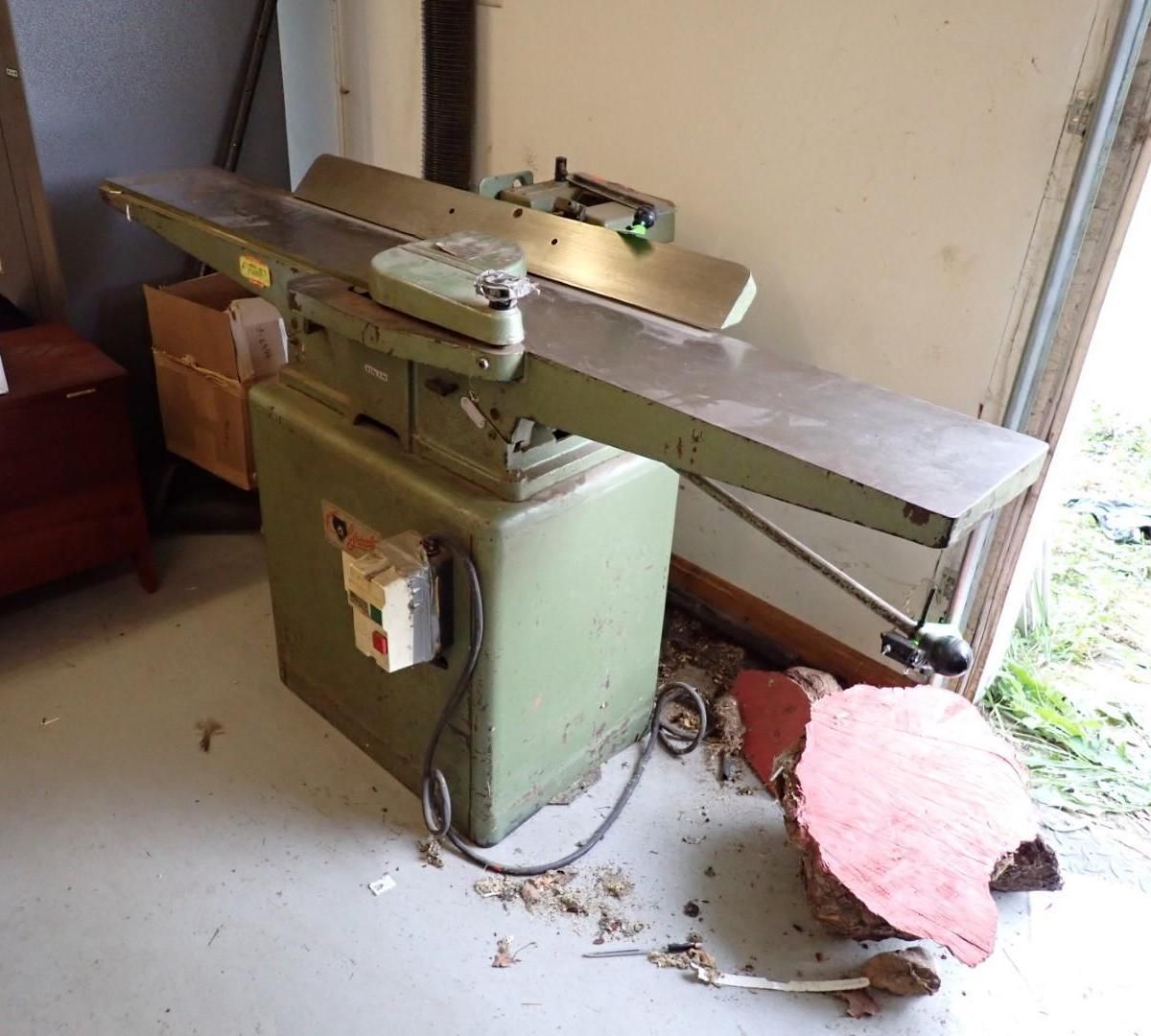 Green woodworking jointer machine in a workshop, with long tables and control panel.