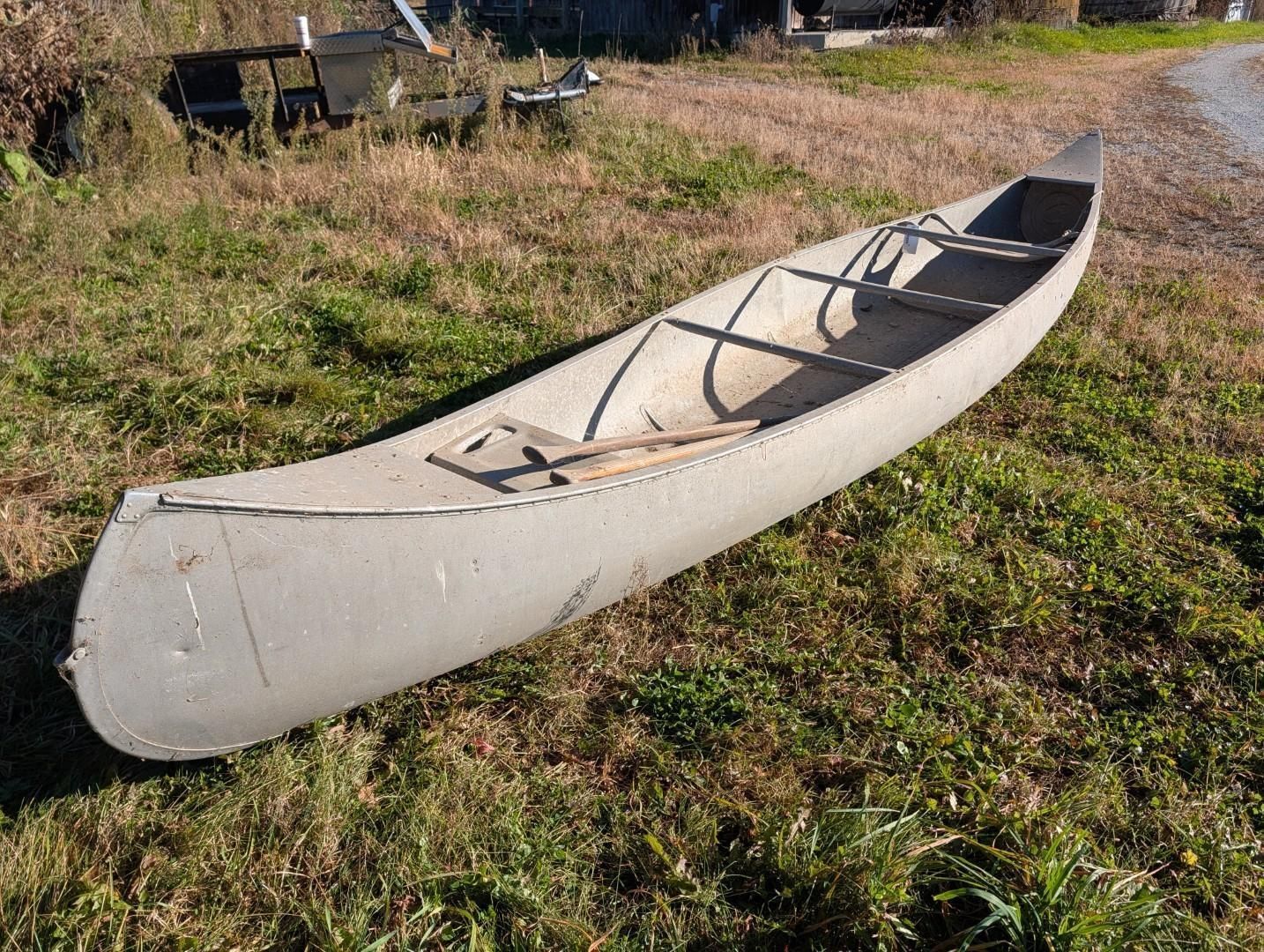 Beige canoe resting on grass beside a gravel path.