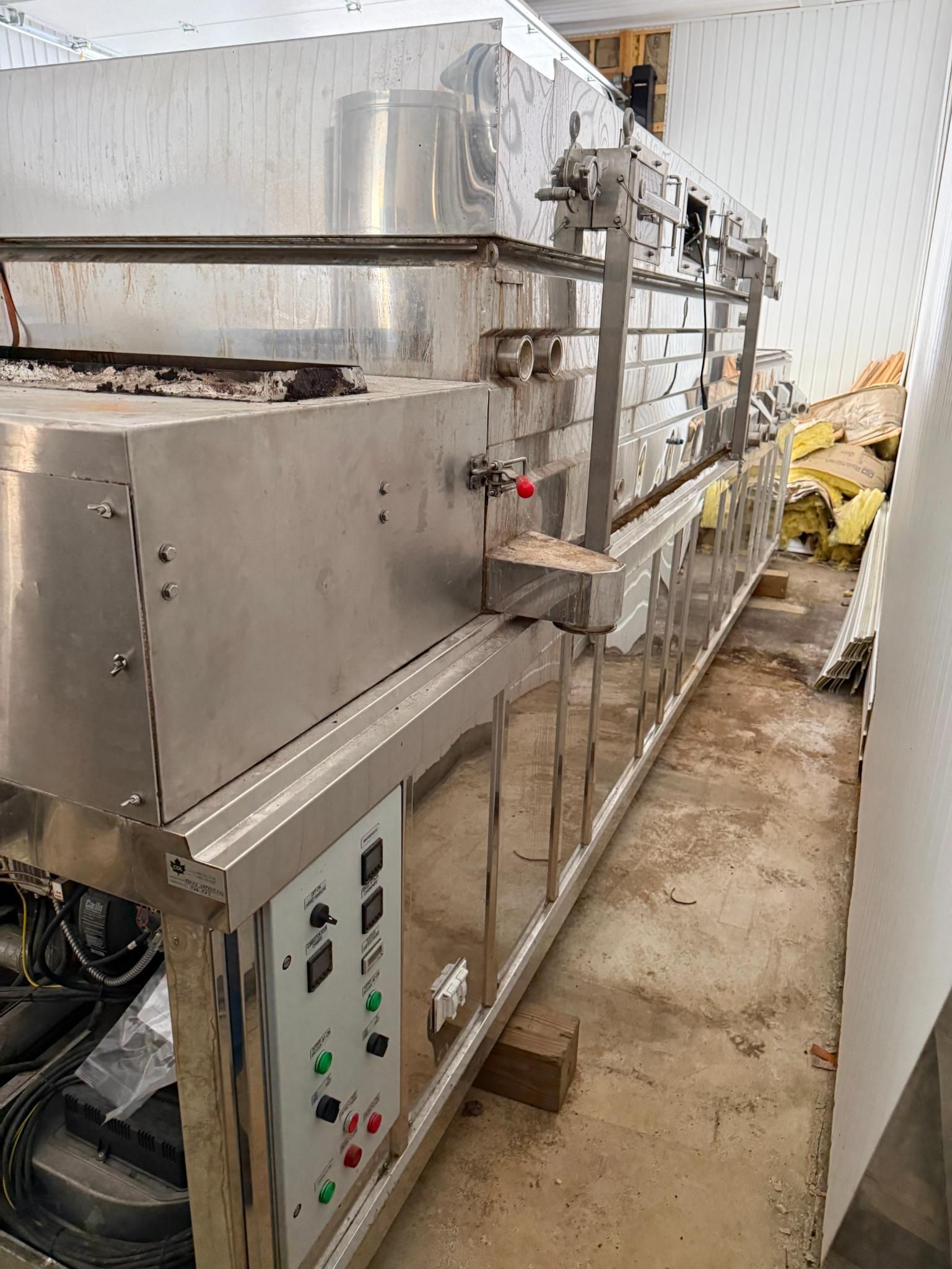 Stainless steel industrial food oven with control panel in a room with a concrete floor.