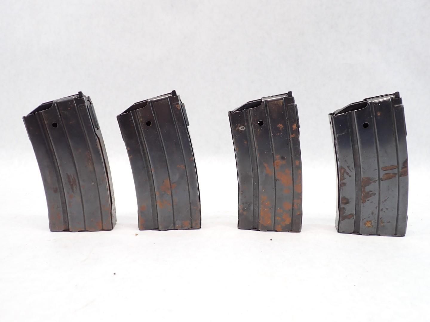 Four dark metal rifle magazines on a white surface.