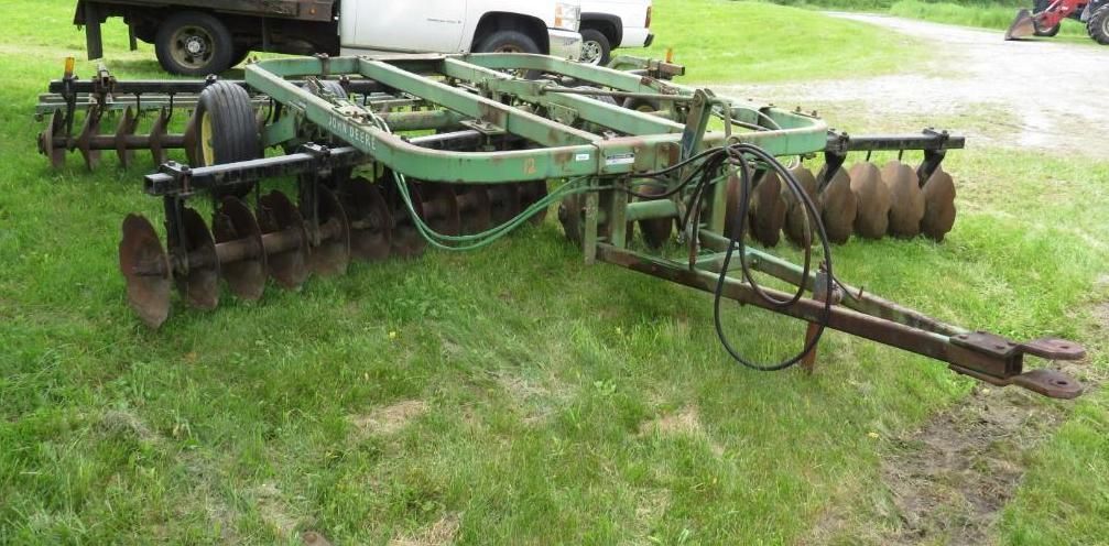 A green John Deere disc harrow, parked on grass.
