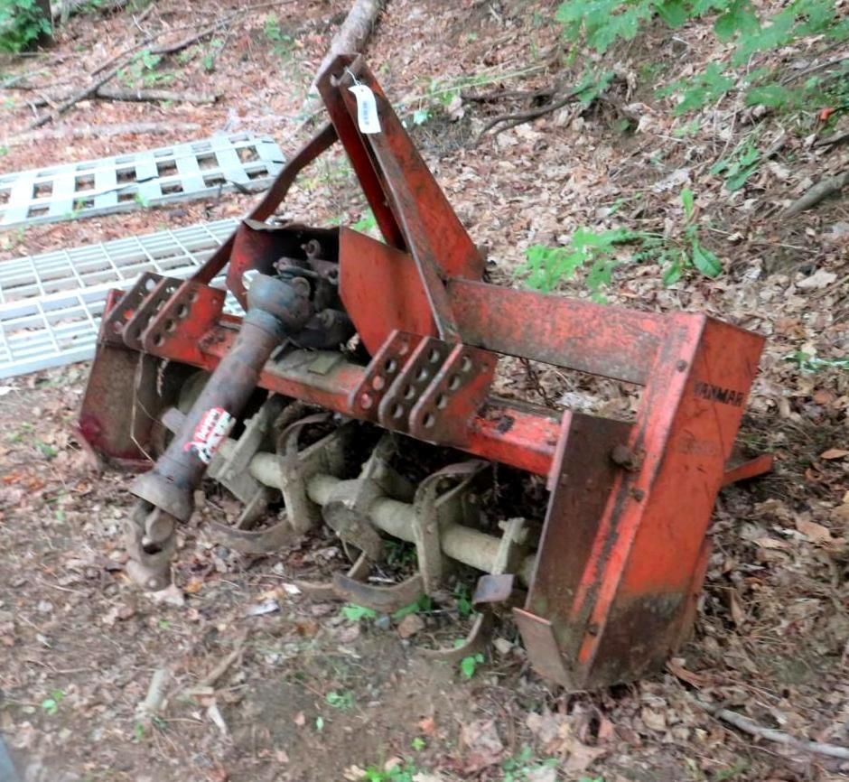 Red rotary tiller in a wooded area.