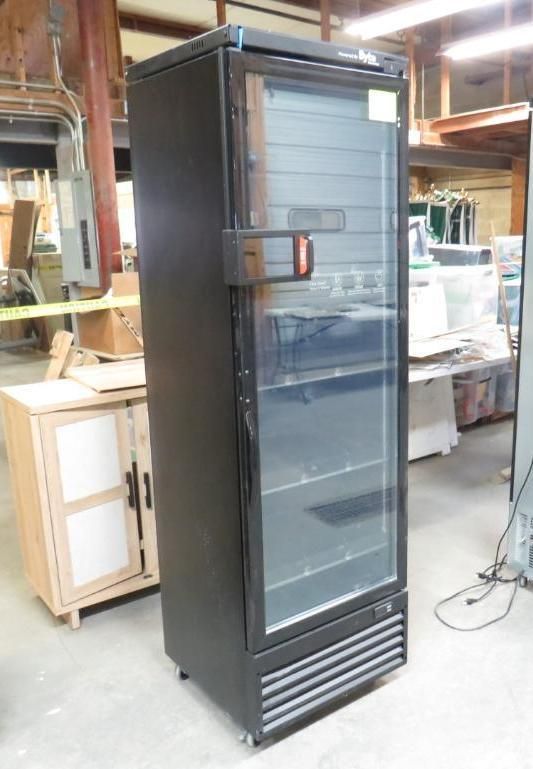 Black commercial refrigerator with glass door in a workshop.