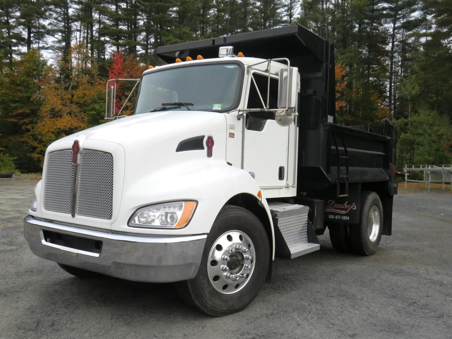 White Kenworth dump truck with black bed, parked outdoors.