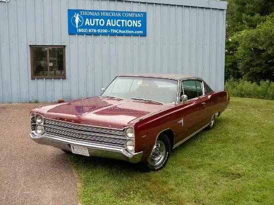 Maroon 1967 Plymouth Fury parked on grass in front of an auto auction building.
