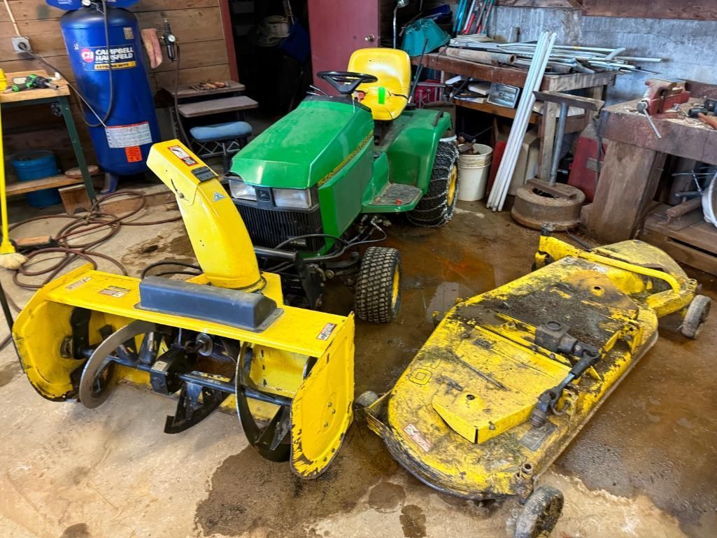 Yellow snowblower, mower deck, and green lawn tractor in a garage.