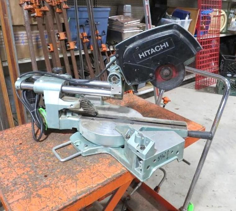 Hitachi miter saw on orange table. Blade covered, silver metal body. Shop background.