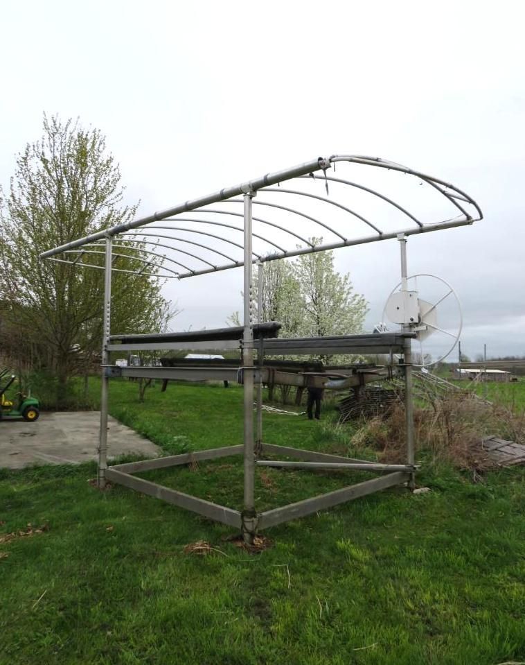 Metal framed greenhouse structure in a grassy field under an overcast sky.