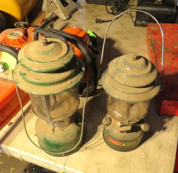 Two green Coleman lanterns on a workbench.
