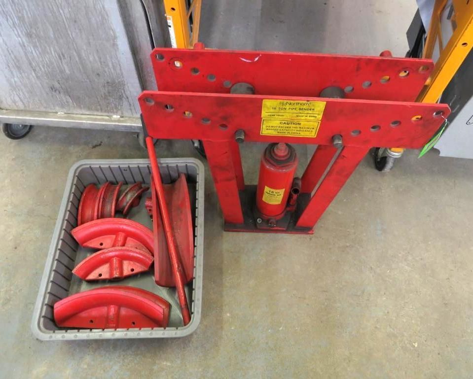 Red hydraulic pipe bender with bending dies in a gray tray.