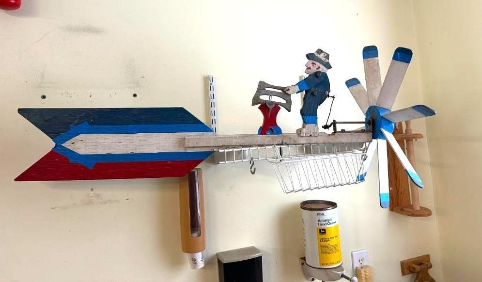 Wooden folk art weather vane with a figure playing an instrument. Blue, white, and red details. Mounted on a wall.