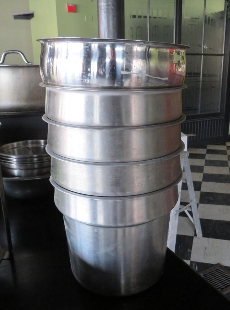 Stack of stainless steel pots and pans on a black surface.