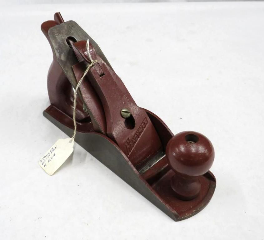 Red hand plane with a wooden knob and metal blade, resting on a white surface.
