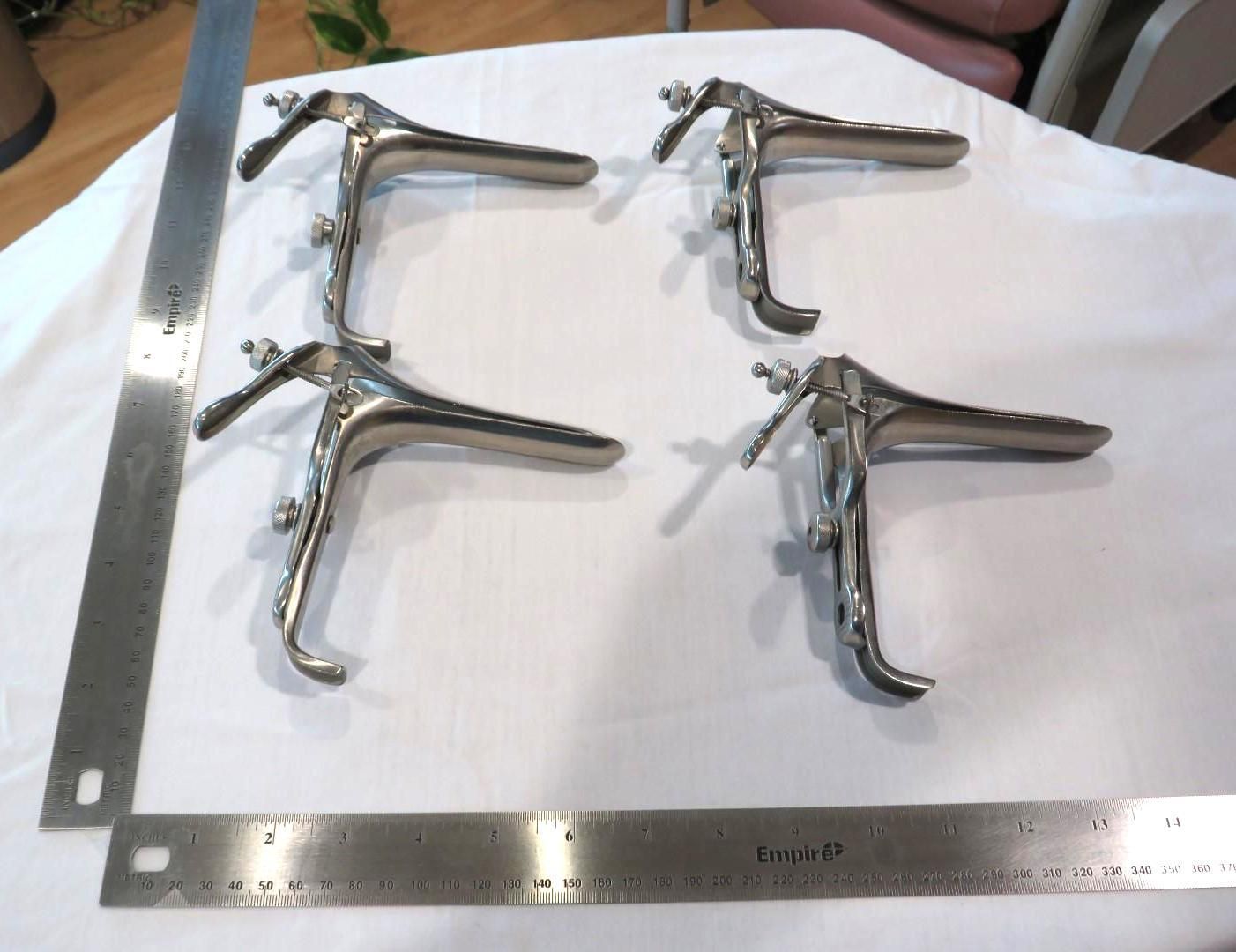 Four metal speculums on white fabric, with two rulers on the sides.