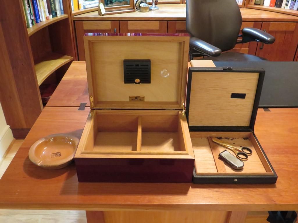 Two open wooden humidors with cigar accessories on a wooden desk.
