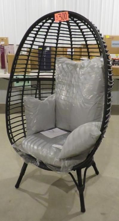 Black wicker egg chair with gray cushions, in a warehouse setting.