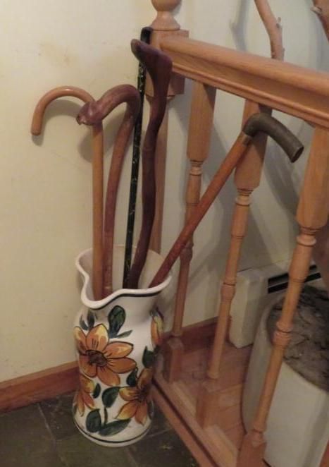 Walking canes in a decorative vase next to wooden stairs and a railing.