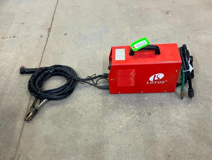 Red Lotos brand welding machine with black cables and clamp on a concrete surface.