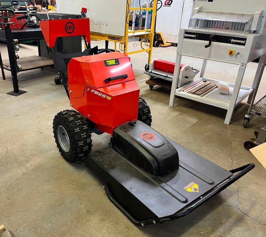 Red and black robotic lawn mower with large tires in a workshop setting.