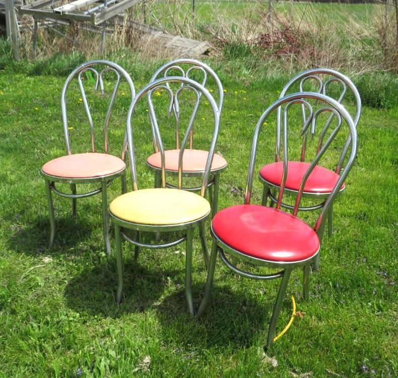 Six vintage metal chairs with colorful seats on a grassy lawn.