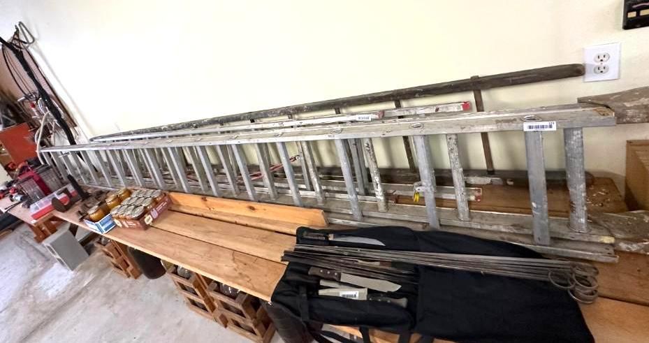 A long, silver aluminum ladder resting on a wooden table, with other items nearby.