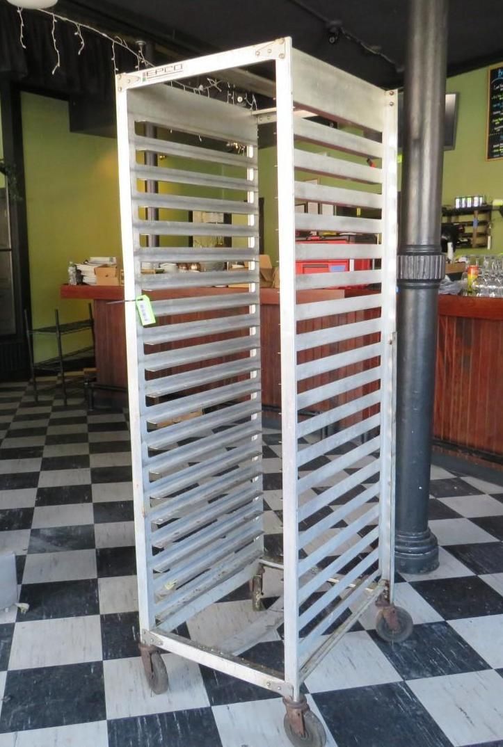 Tall, metal rack on wheels with many horizontal shelves, outdoors in front of a cafe.