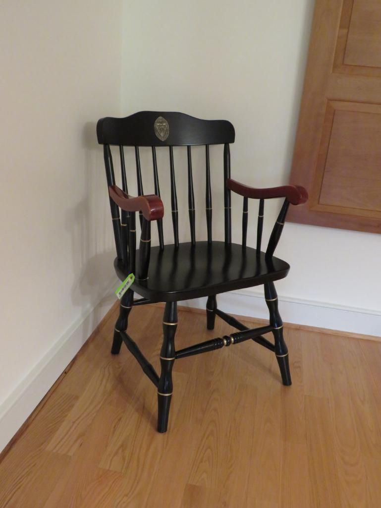 Black wooden arm chair with gold accents; set against white walls and a light wood floor.