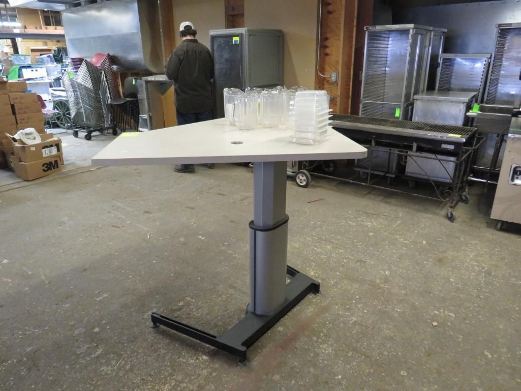 Gray adjustable-height table with clear plastic cups on top, indoors.