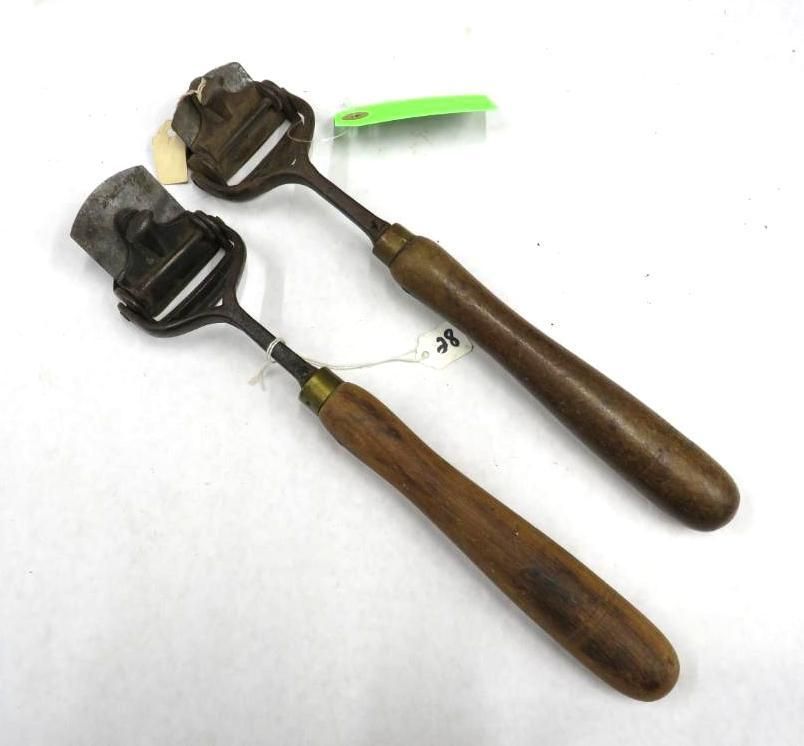 Two wooden-handled leather working tools on a white background. Each has a blade within a metal frame.