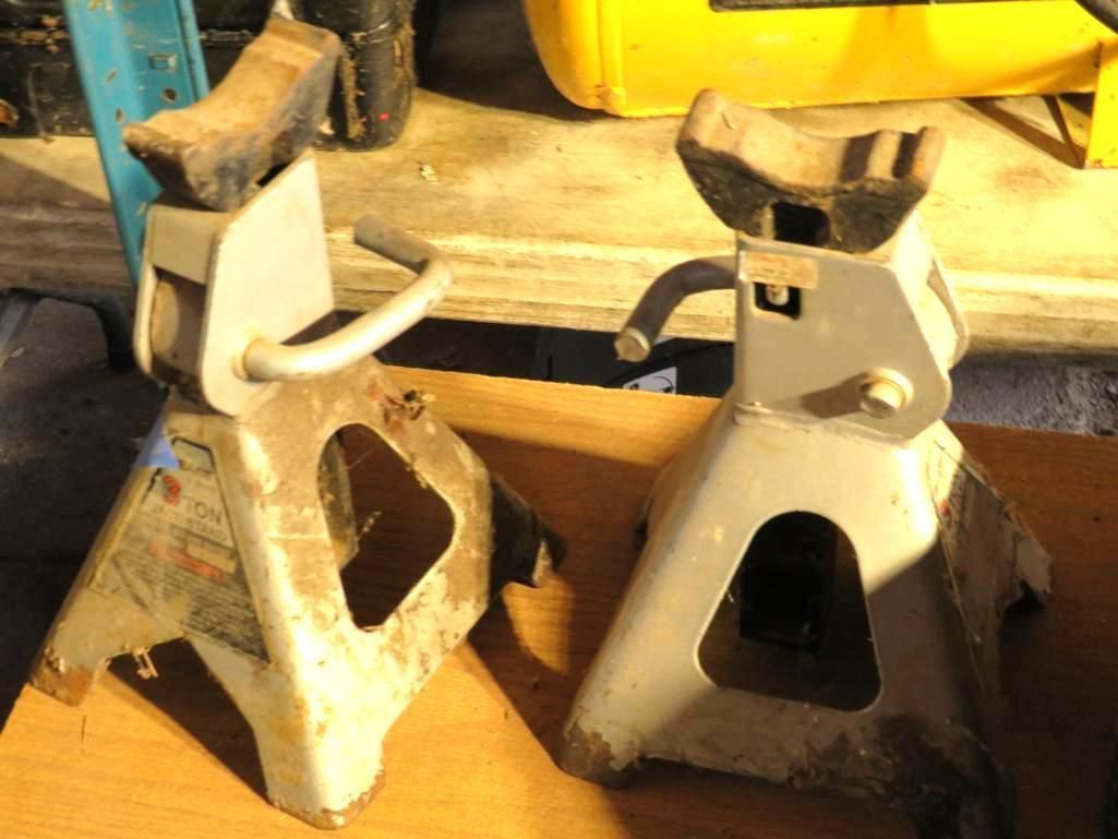 Two gray metal jack stands, angled, with support arms, on a surface.