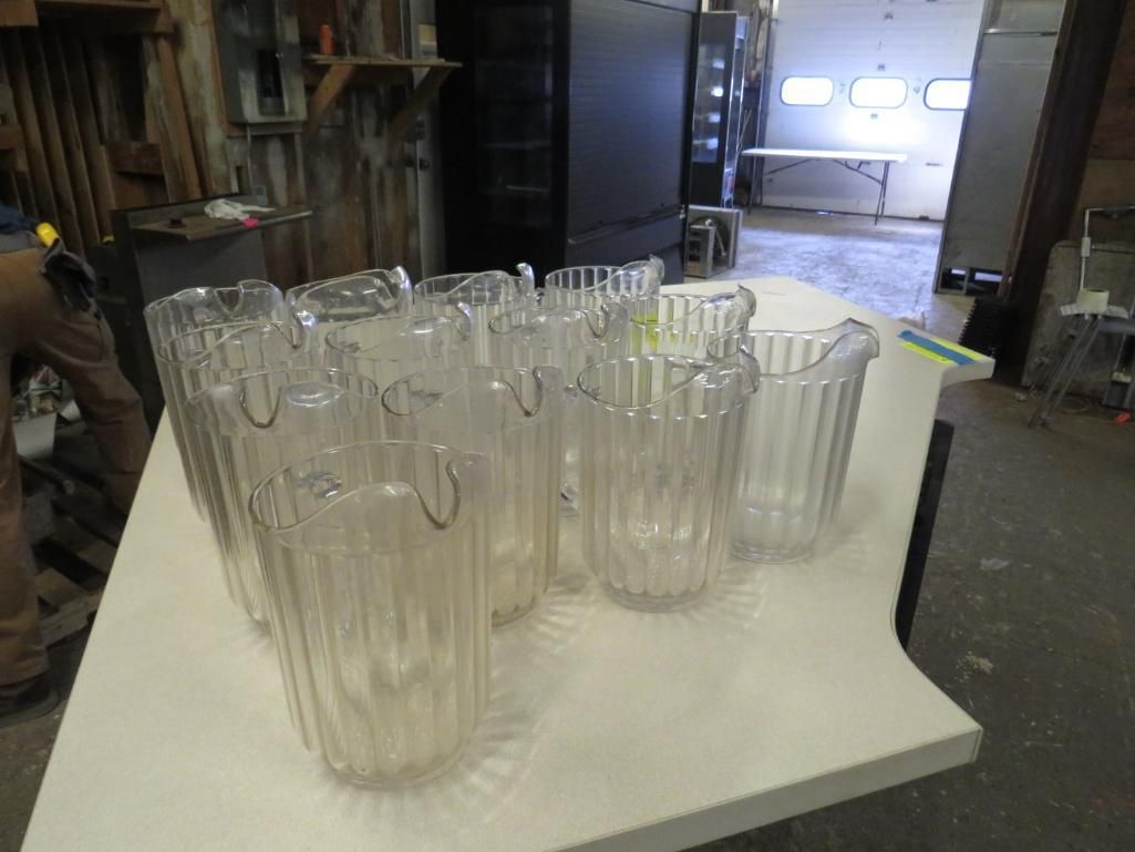 Clear plastic pitchers on a white surface in a workshop setting.
