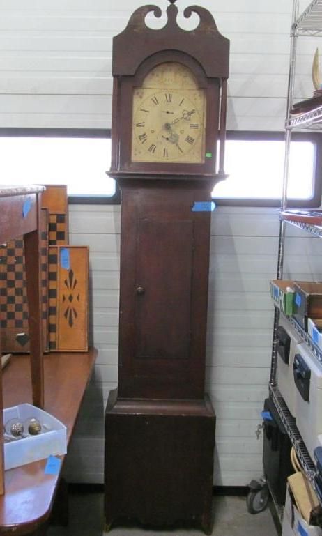 Tall, wooden grandfather clock with a light-colored face and ornate top, standing indoors.