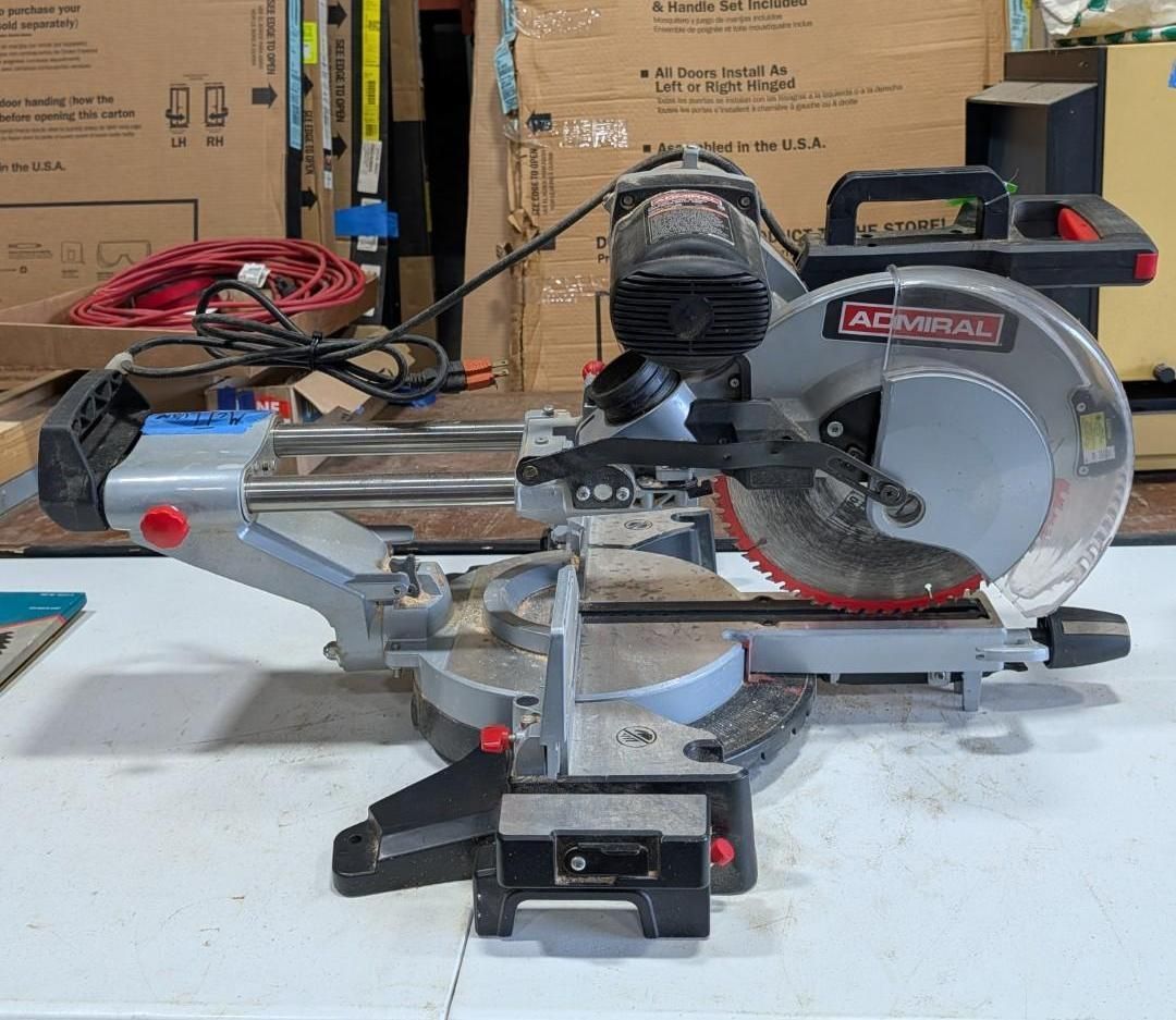 DeWalt miter saw on a workbench in a workshop, with cardboard boxes and tools in the background