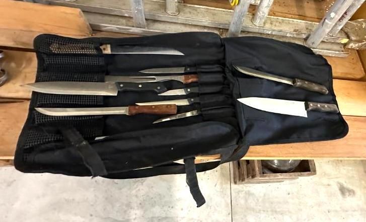 Black knife roll with several knives displayed, open on a wood surface.