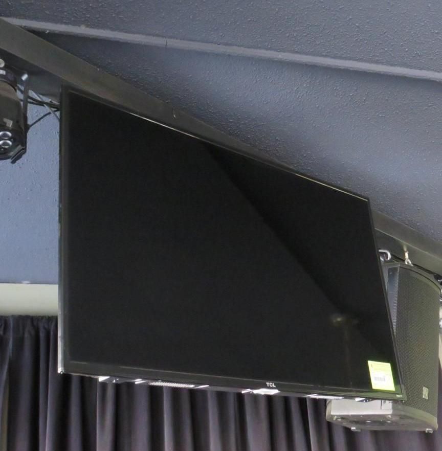 Large, black flat-screen television mounted to a black ceiling beam. A speaker is attached below the television.