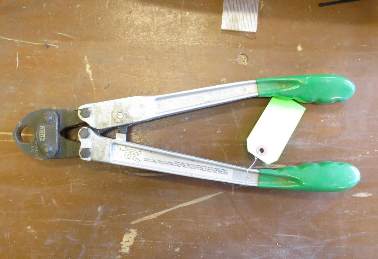 Cable cutter tool with green handles on a wooden surface.
